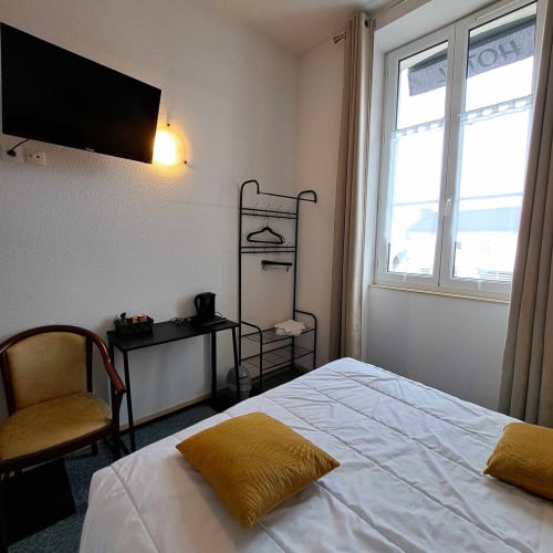 Chambre d'hôtel aux Deux Porches à Verrières avec lit, bureau, chaise et portes-fenêtres sur balcon