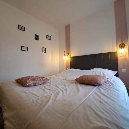 Chambre moderne de l'hôtel Les Deux Porches à Verrières avec linge blanc, tête de lit noire et luminaires suspendus en laiton