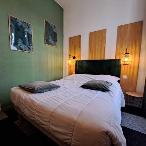 Chambre moderne aux Deux Porches avec murs verts, tête de lit noire, literie blanche, panneaux bois et luminaires suspendus