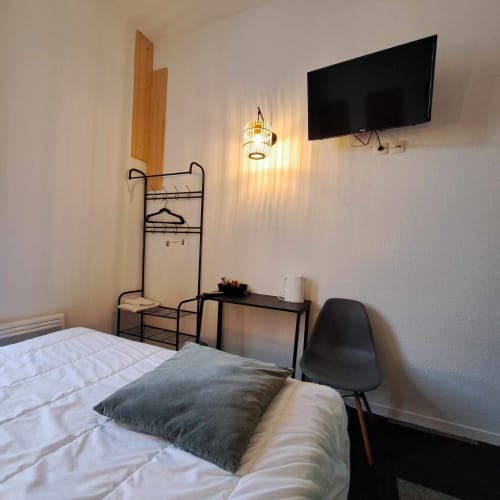 Chambre moderne de l'hôtel Les Deux Porches à Verrières avec lit, bureau, portant, télévision et éclairage décoratif
