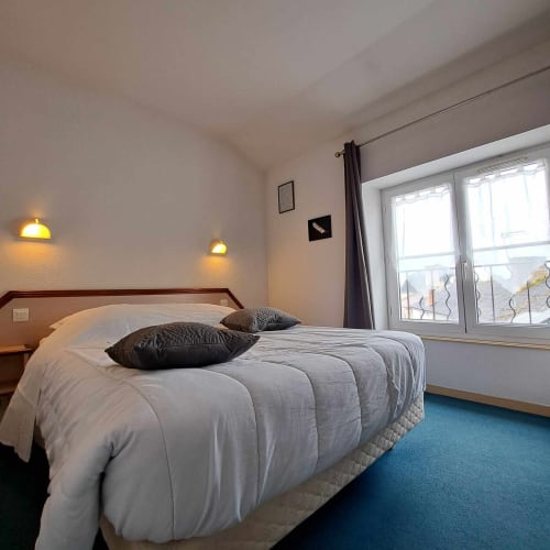 Chambre moderne aux Deux Porches à Verrières avec lit queen-size, oreillers noirs, appliques murales et portes-fenêtres vitrées