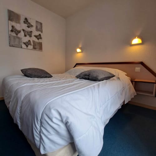 Chambre accueillante aux Deux Porches à Verrières avec lit queen-size, oreillers gris et appliques murales chaleureuses