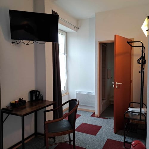 Chambre moderne de l'hôtel Les Deux Porches avec bureau, télévision, porte rouge et vélo d'exercice à Verrières