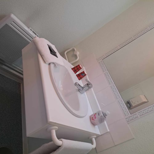 Lavabo immaculé avec meuble blanc, robinet chromé et porte-serviettes à l'hôtel Les Deux Porches à Verrières
