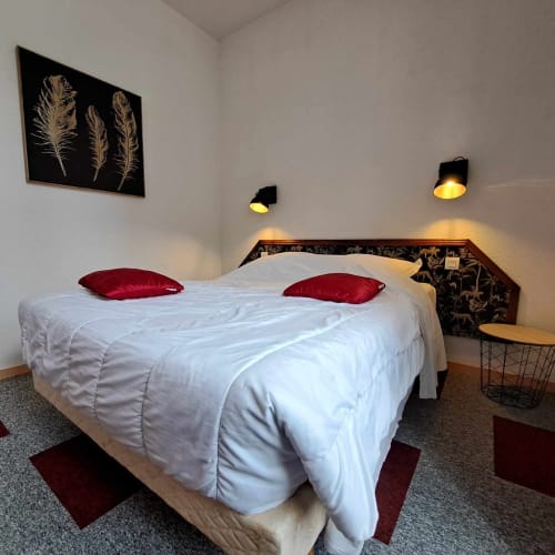 Chambre chaleureuse à l'hôtel Les Deux Porches à Verrières : literie blanche, oreillers rouges, art mural en plumes noires, éclairage ambiant