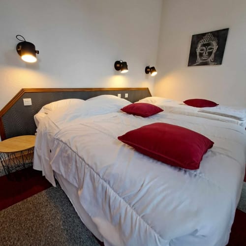 Chambre moderne de l'hôtel Les Deux Porches avec literie blanche, coussins bordeaux et appliques murales noires élégantes