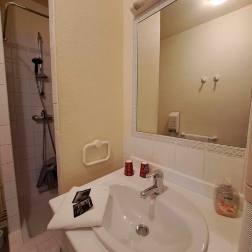 Salle de bain de l'hôtel Les Deux Porches à Verrières avec lavabo, miroir, douche et articles de toilette offerts