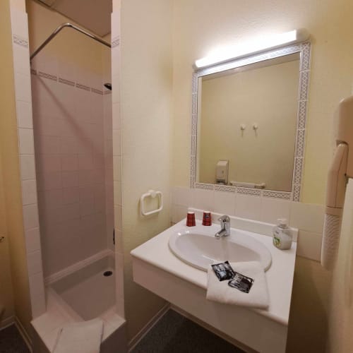 Salle de bain de l'hôtel Les Deux Porches avec lavabo, miroir, douche et équipements