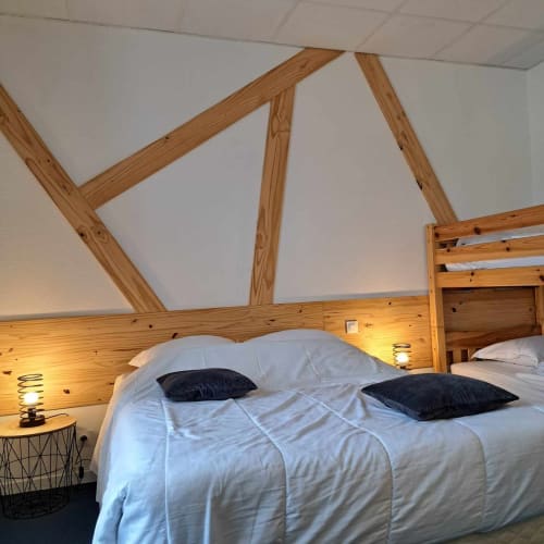 Chambre moderne aux Deux Porches avec poutres en bois, literie blanche, oreillers noirs et éclairage ambiant chaleureux