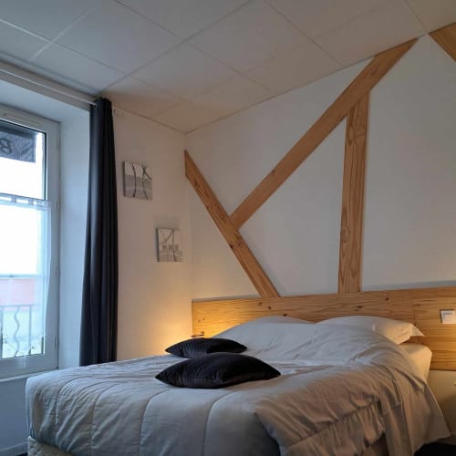 Chambre moderne aux Deux Porches avec lit en bois, literie blanche, oreillers noirs et décoration murale géométrique en bois