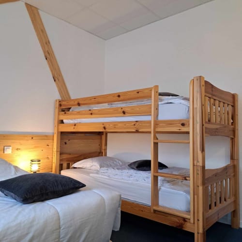 Chambre lumineuse aux Deux Porches avec lit superposé en bois, lit simple, draps blancs, oreillers noirs et petite lampe de bureau
