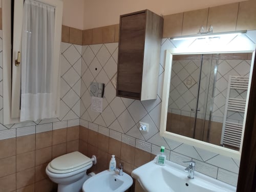 Bagno luminoso nell'appartamento La Maison du Port di Licata, con piastrelle beige, lavabo bianco, bidet, wc e ampia finestra