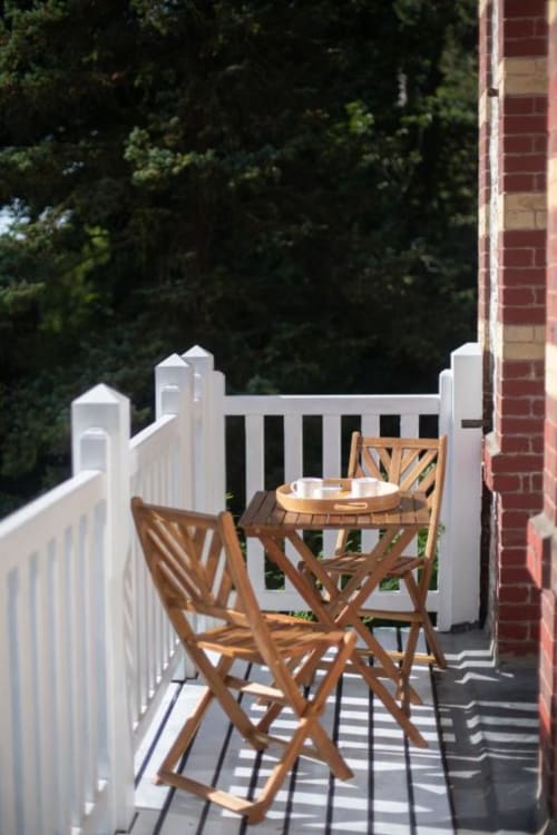Private balcony at Villa Eliane with wooden chairs, small table, white railings overlooking garden in Étretat
