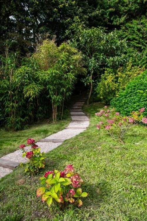 Winding garden pathway at Villa Eliane in Étretat lined with lush greenery, bamboo, and pink flowering shrubs
