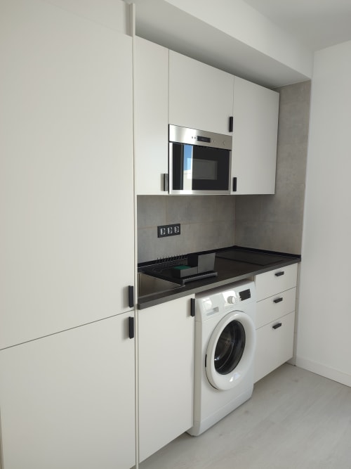 Cocina moderna con muebles blancos, encimera negra, horno integrado y lavadora en El Faro De Los Genoveses