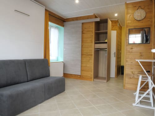 Appartement Sci Saviya à Égletons avec canapé gris, armoire bois, carrelage beige et équipements modernes