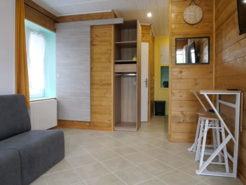 Intérieur de l'appartement Sci Saviya à Égletons avec finitions en bois, kitchenette, canapé et équipements modernes
