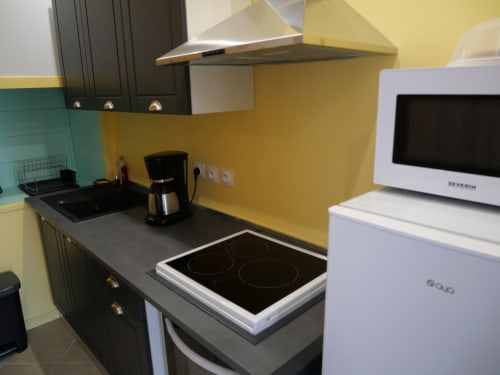 Cuisine moderne de l'appartement Sci Saviya à Égletons avec murs jaunes, placards noirs, cuisinière électrique et micro-ondes blanc