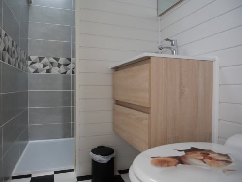 Salle de bain moderne de l'appartement Sci Saviya à Égletons avec meuble vasque en bois, douche carrelée grise et sol bicolore noir et blanc