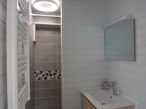 Salle de bain moderne de l'appartement Sci Saviya à Égletons avec douche, lavabo, miroir et carrelage blanc