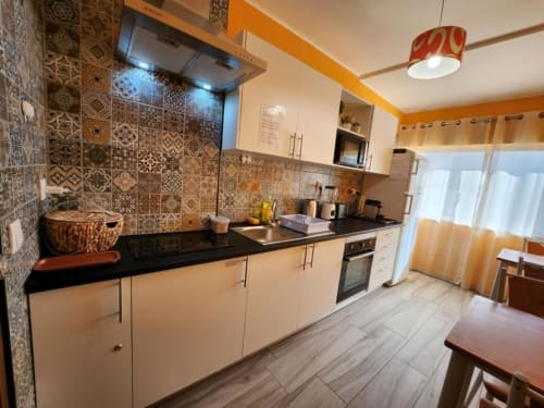 Modern kitchen with ornate tile backsplash, black counters, and warm orange accents at Casa do Sol Algarve hotel in Lagos,