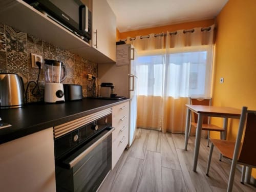 Modern kitchen with orange walls, black counters, dining table at Casa do Sol Algarve hotel in Lagos