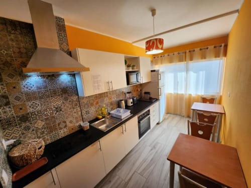 Cozinha moderna em Casa do Sol Algarve Lagos com detalhes em laranja, azulejos estampados no painel traseiro e móveis de jantar em madeira