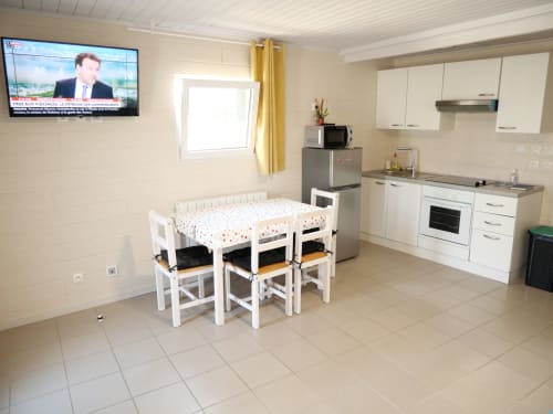 Cuisine-salle à manger de l'appartement Sci Saviya à Égletons avec table blanche, chaises et kitchenette équipée