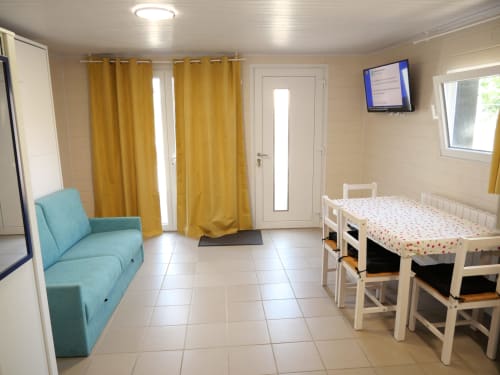 Appartement lumineux au Sci Saviya B&B à Égletons avec canapé turquoise, lit blanc, rideaux jaunes et télévision