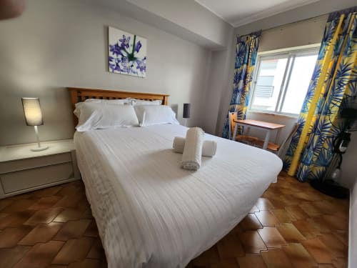 Quarto duplo luminoso em Casa do sol Algarve, Lagos com roupa de cama branca, cabeceira de madeira e cortinas com padrão azul