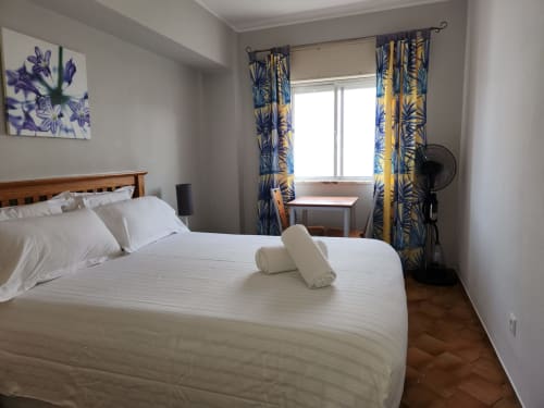 Bright double bedroom at Casa do Sol Algarve in Lagos with white bedding, blue and yellow curtains, wooden furniture, and