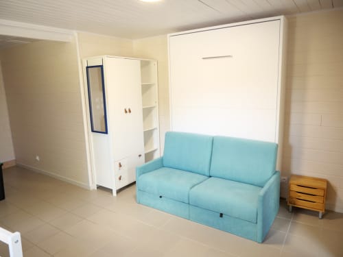 Studio lumineux Sci Saviya avec canapé turquoise, lit escamotable, rangements blancs et table de nuit en bois