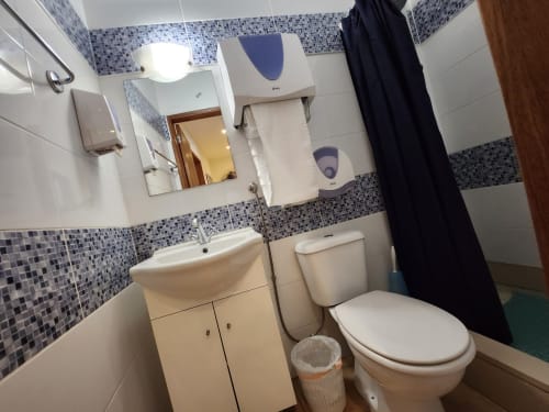 Banheiro compartilhado na Casa do Sol Algarve Lagos com pia, vaso sanitário, chuveiro com cortina preta e azulejos de mosaico azul