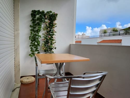 Varanda externa da Casa do sol Algarve em Lagos com mesa de madeira, cadeiras metálicas e videiras floridas contra parede branca
