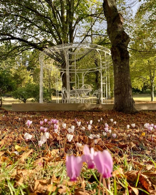 White wrought iron gazebo surrounded by pink and white flowers at Domaine de Bize, Mirepoix mansion