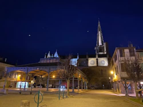 Place historique de Mirepoix illuminée la nuit avec clocher d'église brillant et bâtiments architecturaux