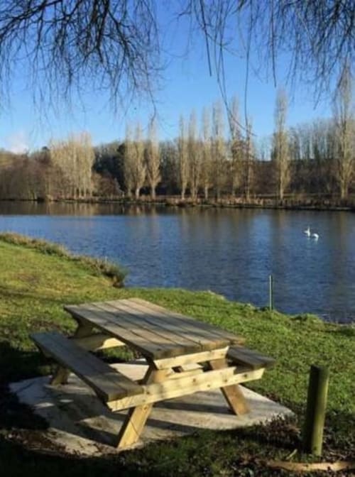 Table de pique-nique avec vue sur le lac paisible et les saules pleureurs aux Deux Porches, Verrières