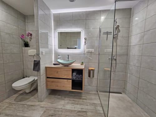 Modern bathroom at Domaine à l'Aise with walk-in shower, wooden vanity, glass basin sink, and illuminated mirror in
