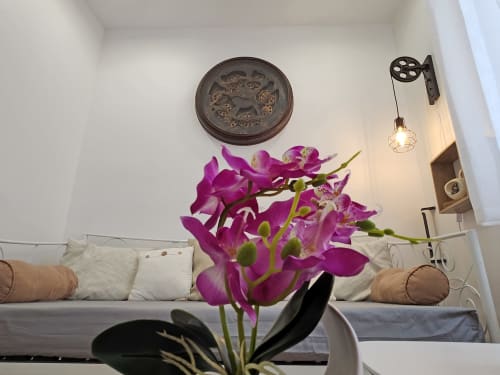 Elegant bedroom at Domaine à l'Aise with vibrant purple orchids, decorative wall plaque, and modern pendant lighting above a