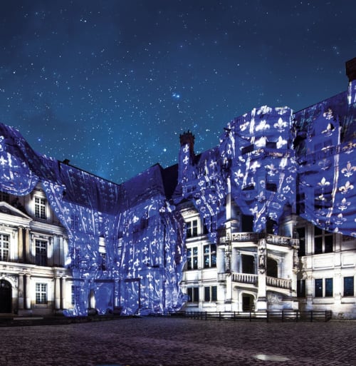 Château de Blois illuminé la nuit avec projections de fleurs de lis bleues et ciel étoilé