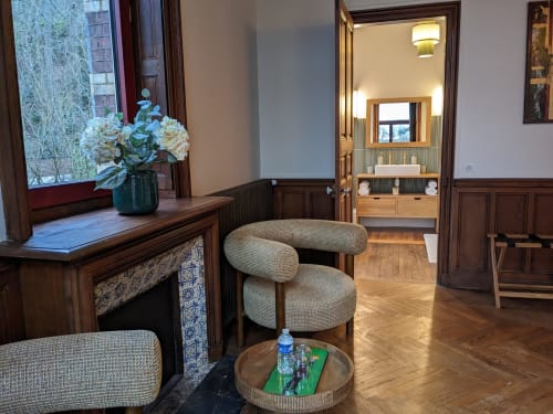 Elegant sitting area with curved beige chair, wooden furnishings, and floral arrangement at Villa Eliane boutique hotel in
