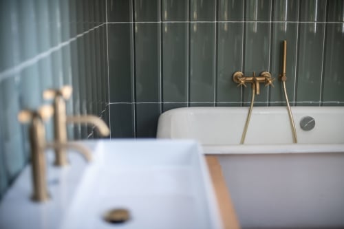 Modern bathroom with gold fixtures, white sink and bathtub, dark green tile wall at Villa Eliane in Étretat