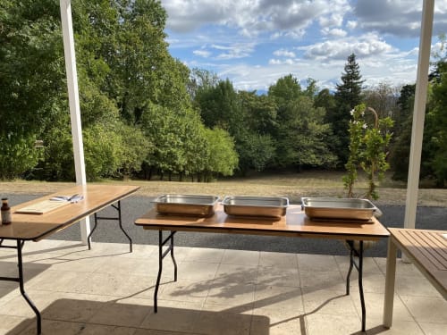 Outdoor catering setup at Domaine de Bize Mirepoix with metal trays on wooden tables, mountains and green trees in background