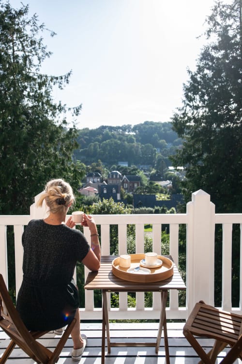 Woman enjoying coffee on balcony overlooking Étretat countryside at Villa Eliane deluxe room