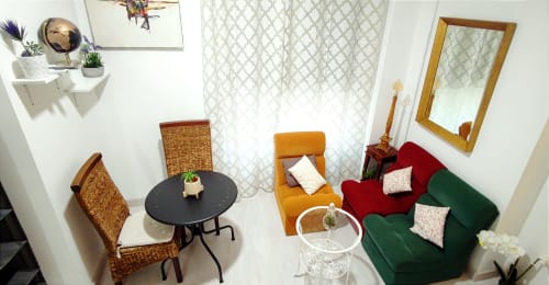 Sala de Apartamentos Huelintown con sofás verdes y rojos, mesa negra y sillas tejidas en Málaga