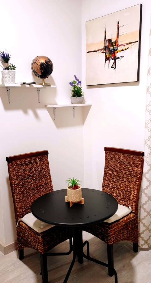 Rincón moderno de habitación en Apartamentos Huelintown, Málaga, con mesa redonda, sillas de mimbre, estantes, globo terráqueo y plantas