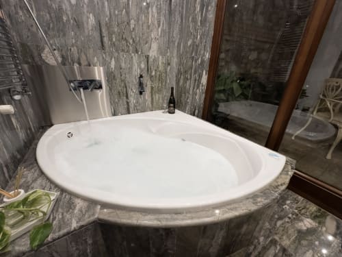 Bañera circular blanca moderna con paredes de piedra gris y ventana en Suite Comares, Granada