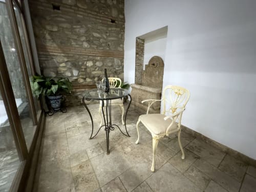 Elegante zona de descanso en la terraza de Suite Comares Granada con butaca crema, mesa de hierro forjado, muros de piedra y elementos decorativos