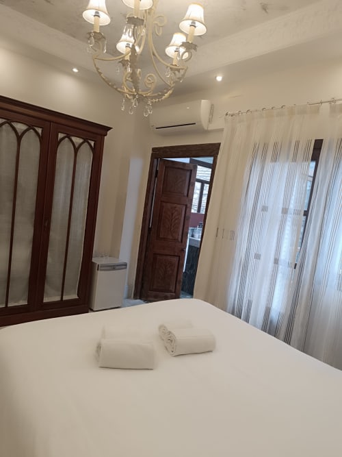 Elegante habitación en Suite Comares Granada con ropa de cama blanca, araña, armario de madera y cortinas translúcidas