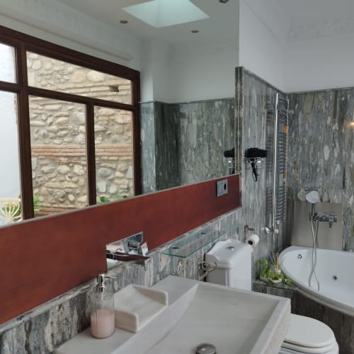 Baño moderno del hotel Suite Comares en Granada con doble lavabo, paredes de azulejos grises, panel rojo decorativo y ducha de efecto lluvia